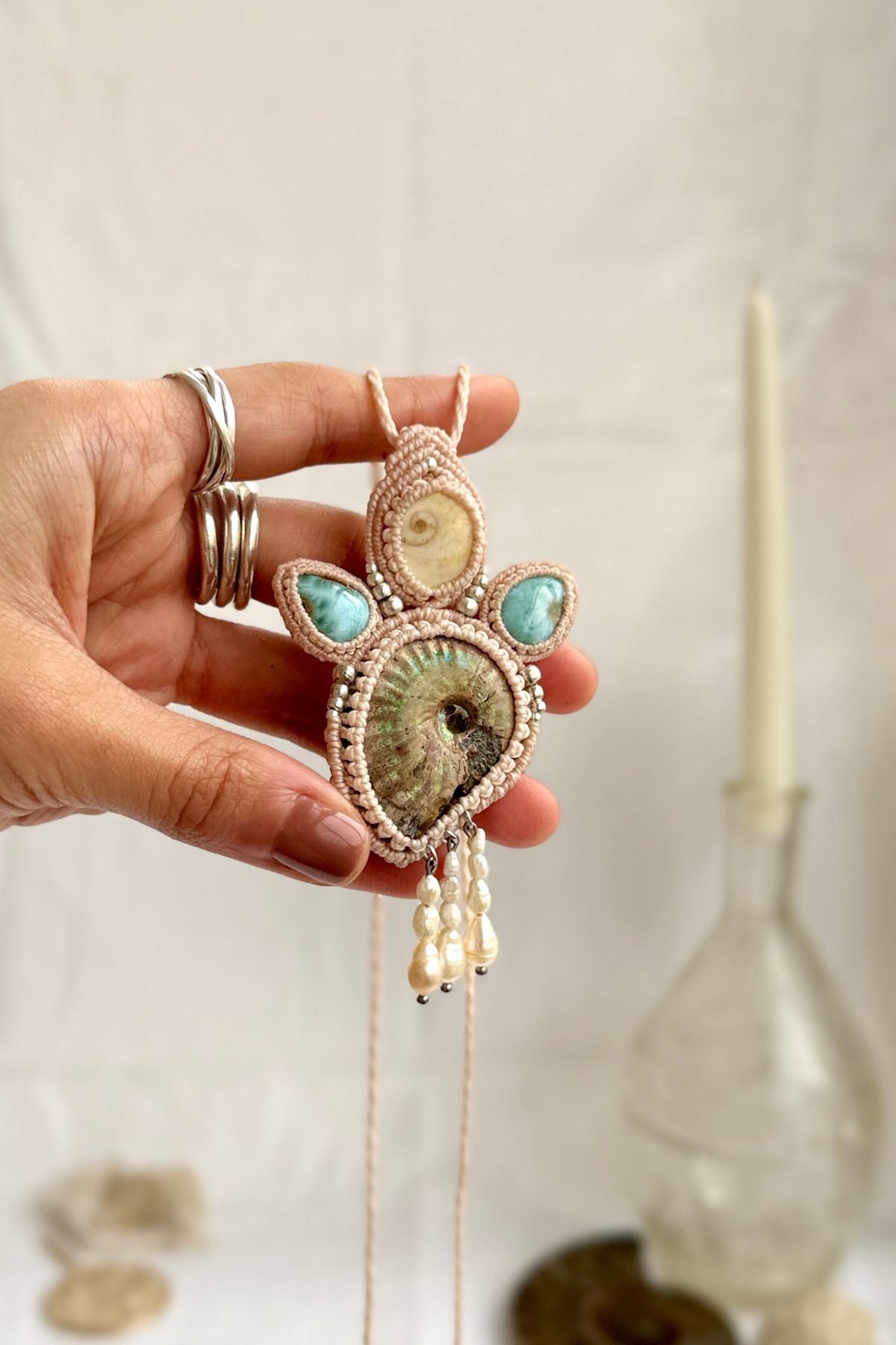 Opalized ammonite fossil necklace with natural operculum and larimar shown in hand