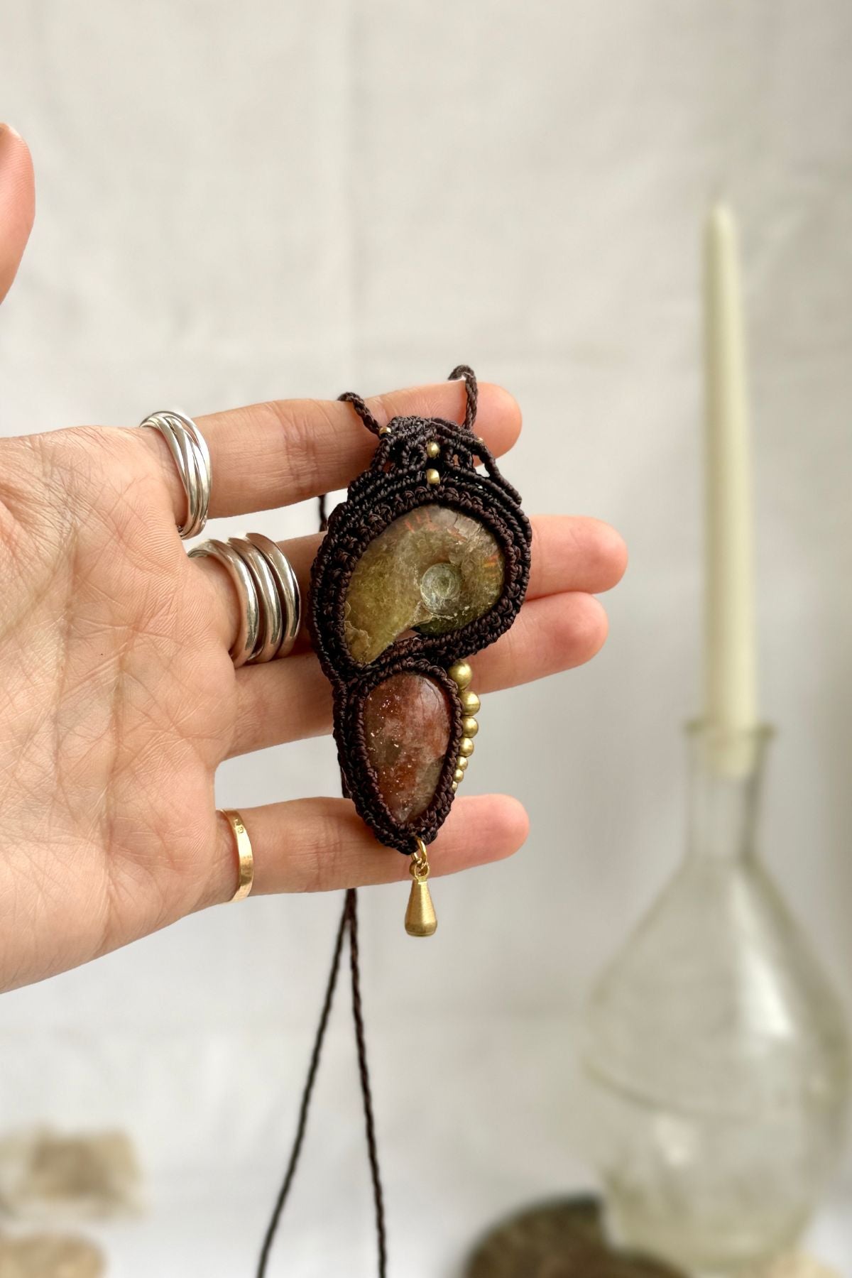 Opalized ammonite and sunstone pendant necklace shown in hand, highlighting natural iridescence and organic design