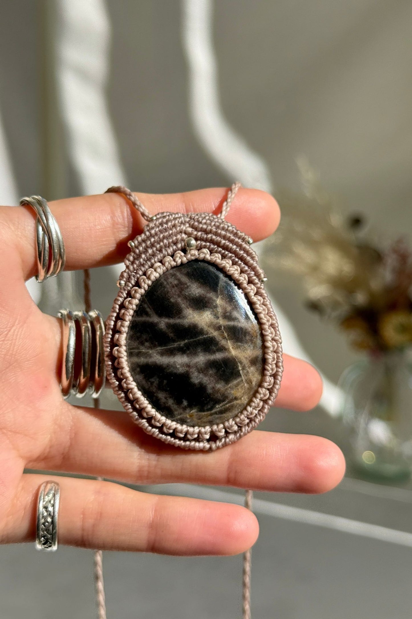 Hand holding a handmade Black Moonstone necklace, highlighting the intricate macrame work and the natural glow of the gemstone.