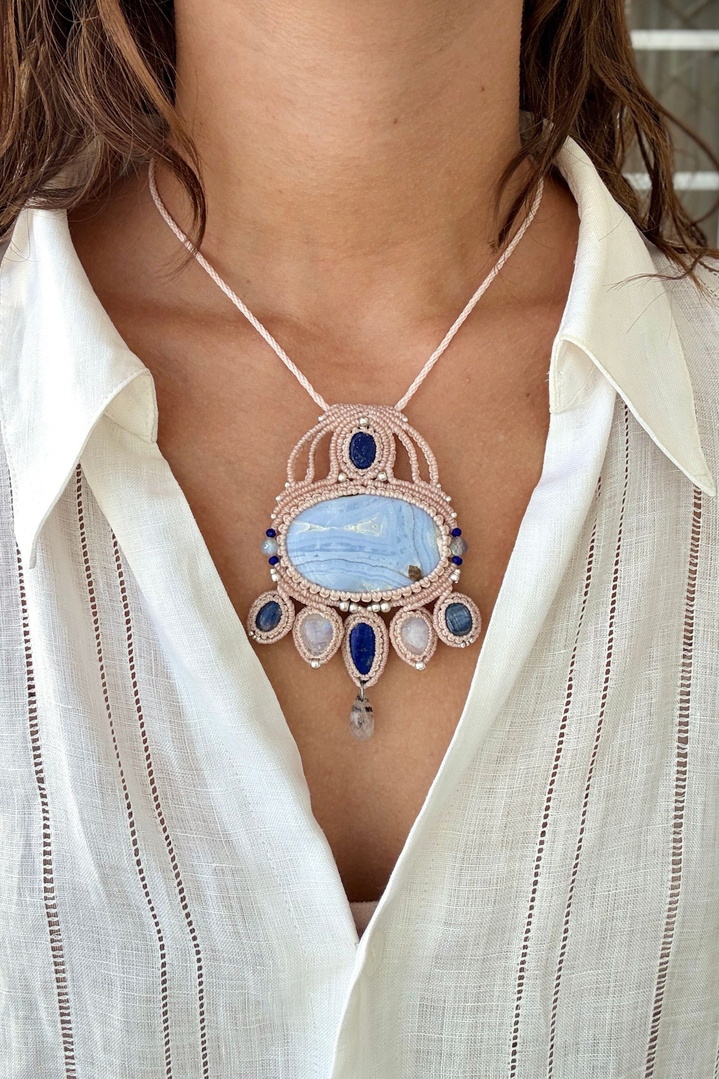 Model wearing a handmade gemstone macrame statement necklace with Blue Lace Agate, Lapis Lazuli, Moonstone, and intricate white cord design