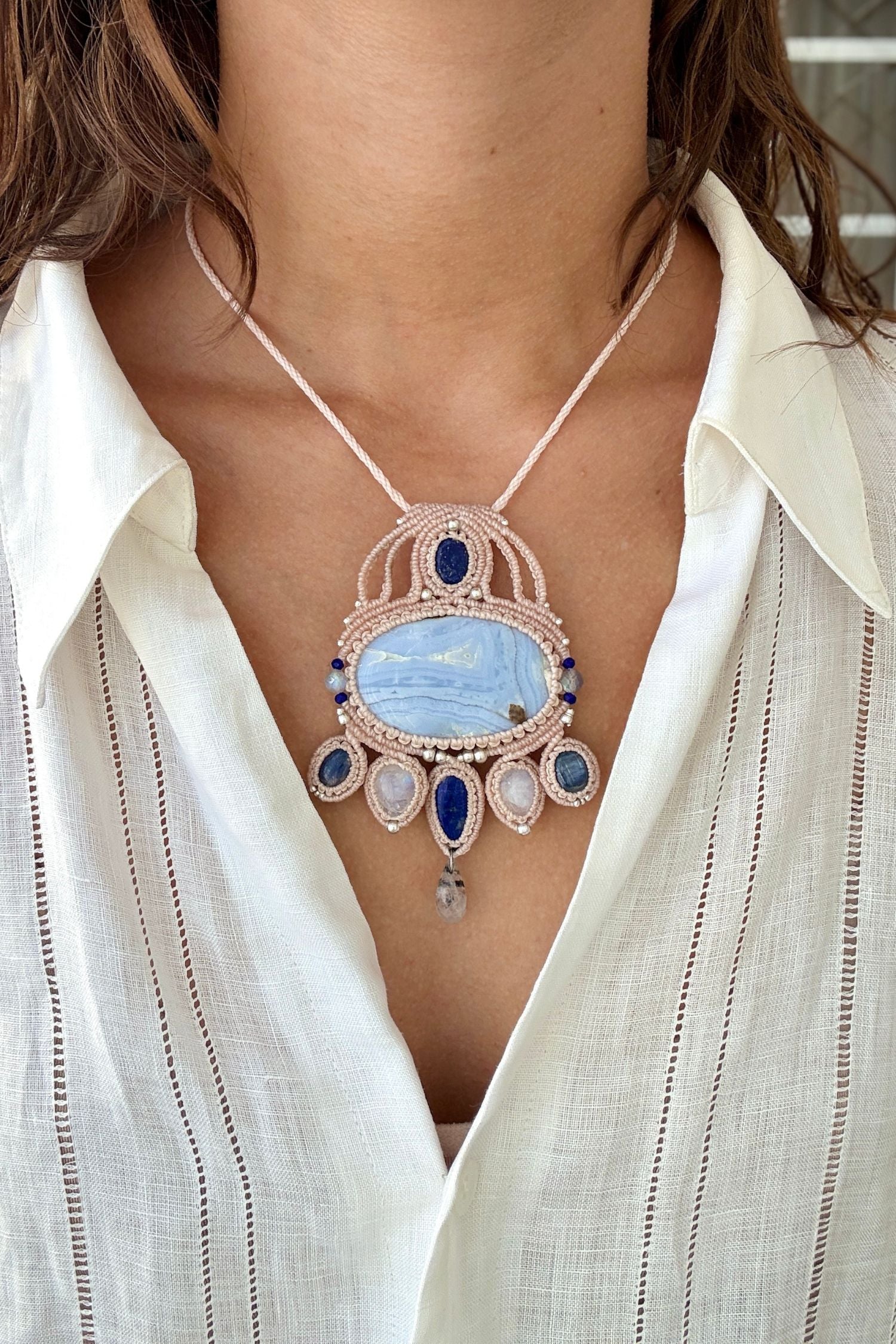 Model wearing a handmade gemstone macrame statement necklace with Blue Lace Agate, Lapis Lazuli, Moonstone, and intricate white cord design