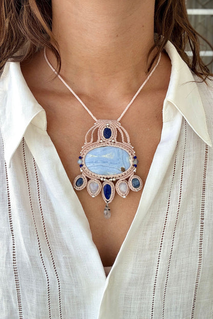 Model wearing a handmade gemstone macrame statement necklace with Blue Lace Agate, Lapis Lazuli, Moonstone, and intricate white cord design
