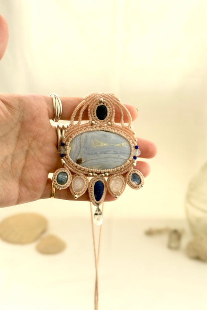 Hand holding a one of a kind macrame necklace with Blue Lace Agate centerpiece and multiple natural gemstones