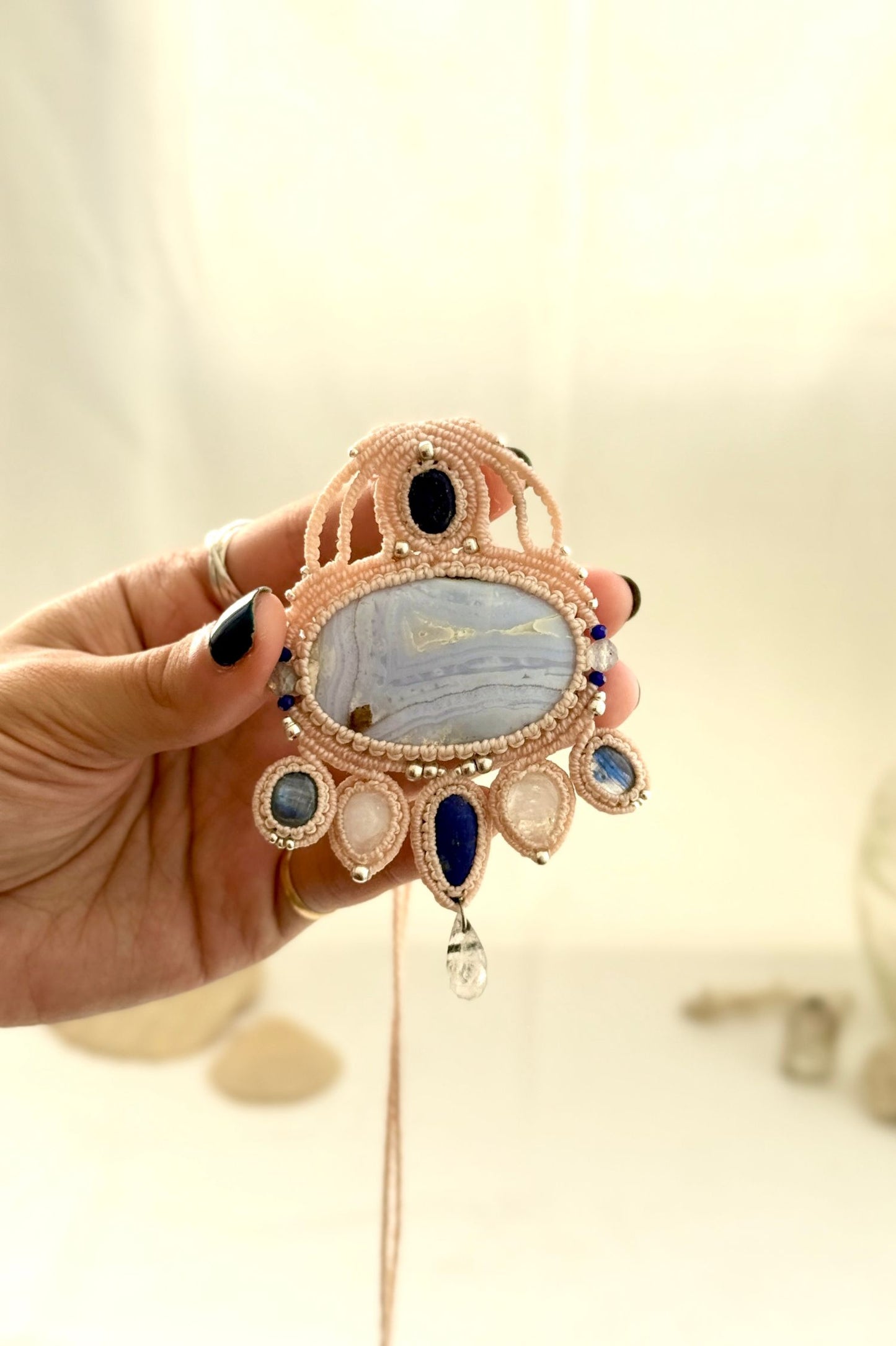 Hand holding a detailed gemstone macrame necklace highlighting intricate knotwork and layered stone composition