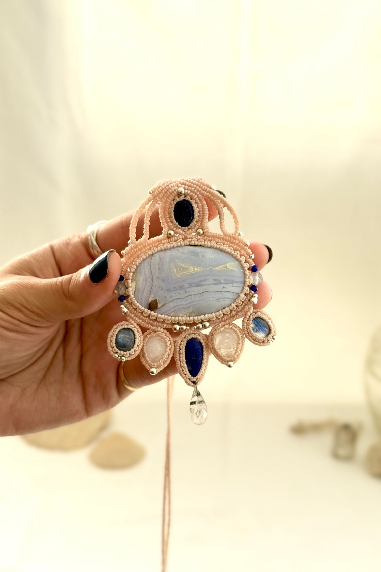 Hand holding a detailed gemstone macrame necklace highlighting intricate knotwork and layered stone composition