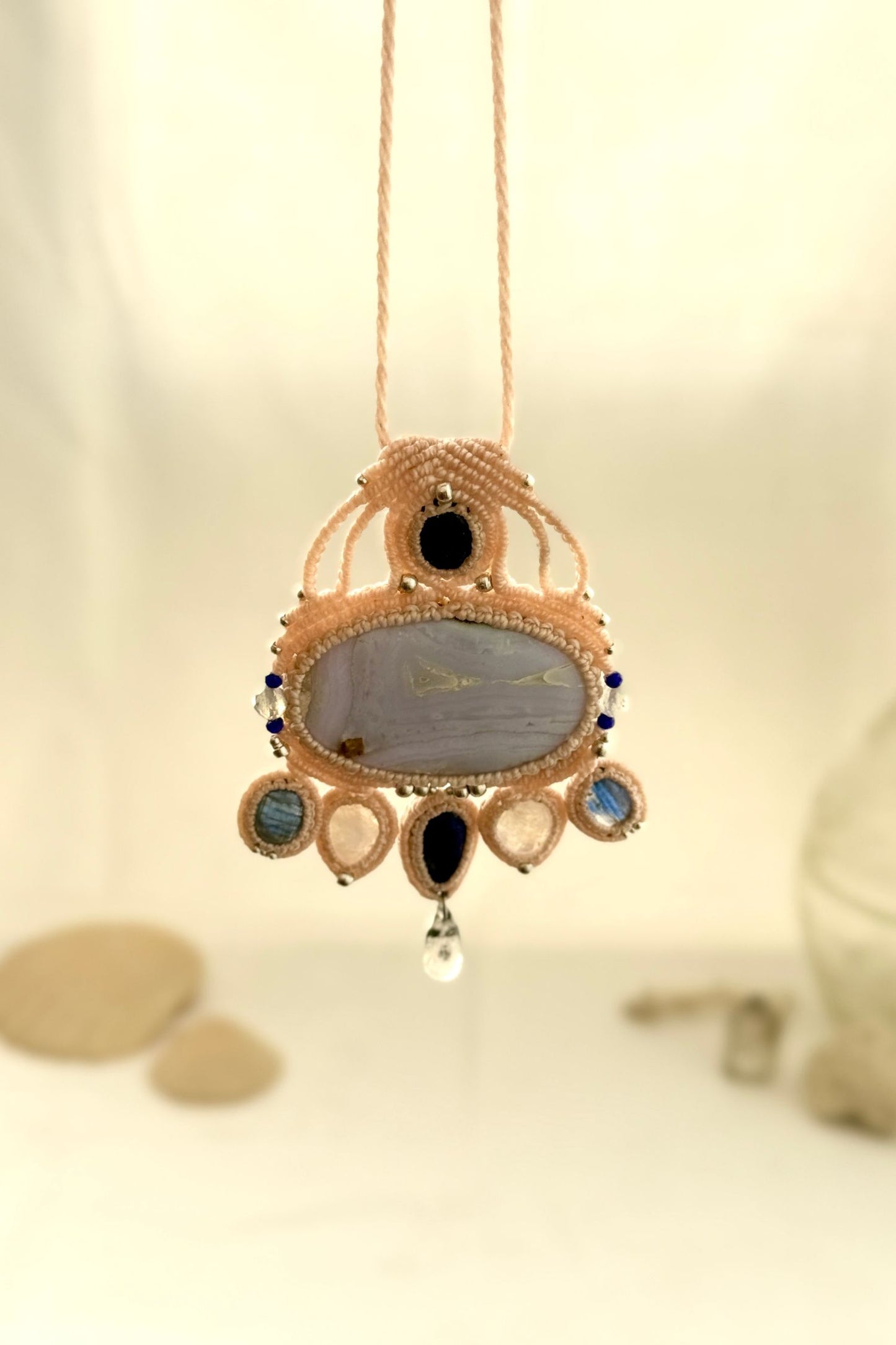 Hanging view of a gemstone macrame necklace showing the transparency and natural textures of Blue Lace Agate, Quartz, and Moonstone