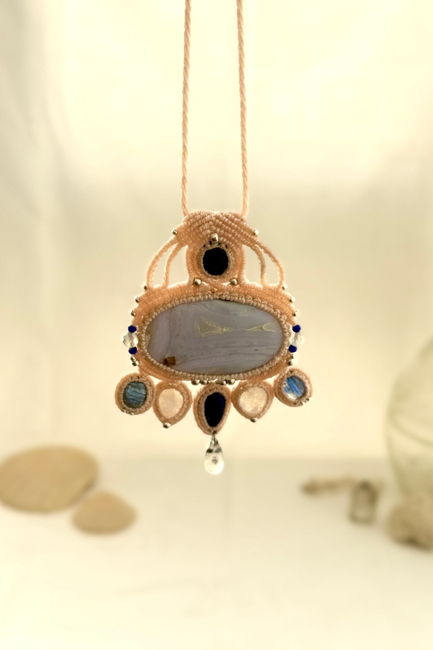 Hanging view of a gemstone macrame necklace showing the transparency and natural textures of Blue Lace Agate, Quartz, and Moonstone
