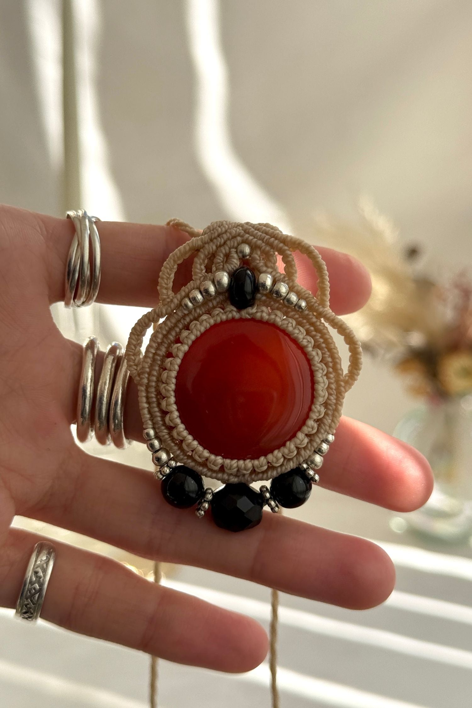 Hand holding a handmade Carnelian and Onyx necklace, highlighting the intricate macrame work and the natural glow of the gemstones.