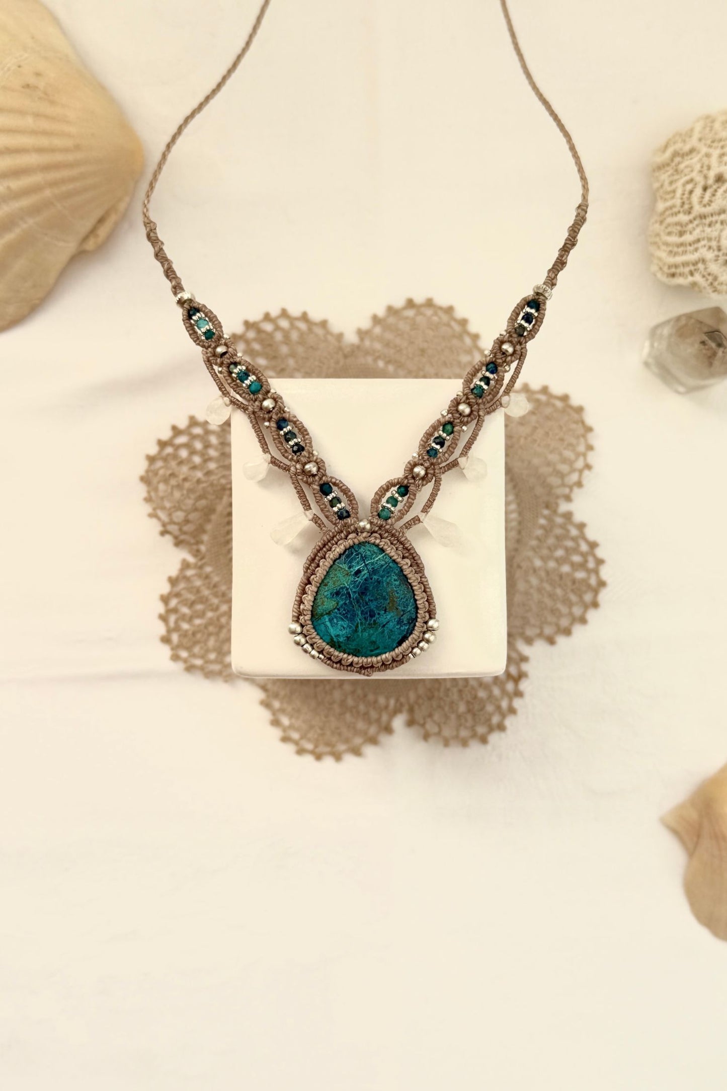 Handmade Chrysocolla macramé necklace laid in a styled setting, highlighting its V-shaped design and earthy blue tones