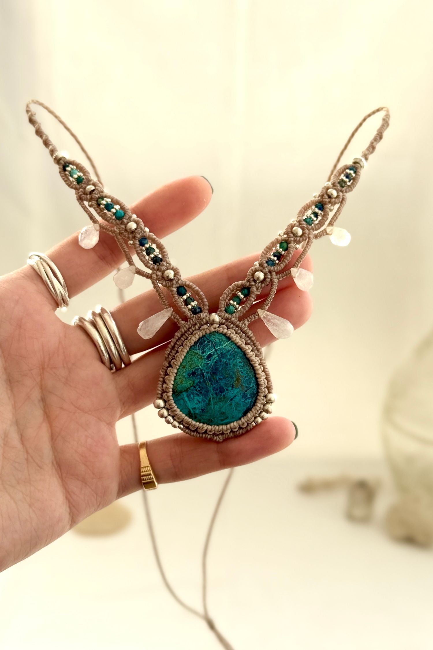 Hand holding a one of a kind Chrysocolla macramé necklace with silver bead details and Moonstone drops