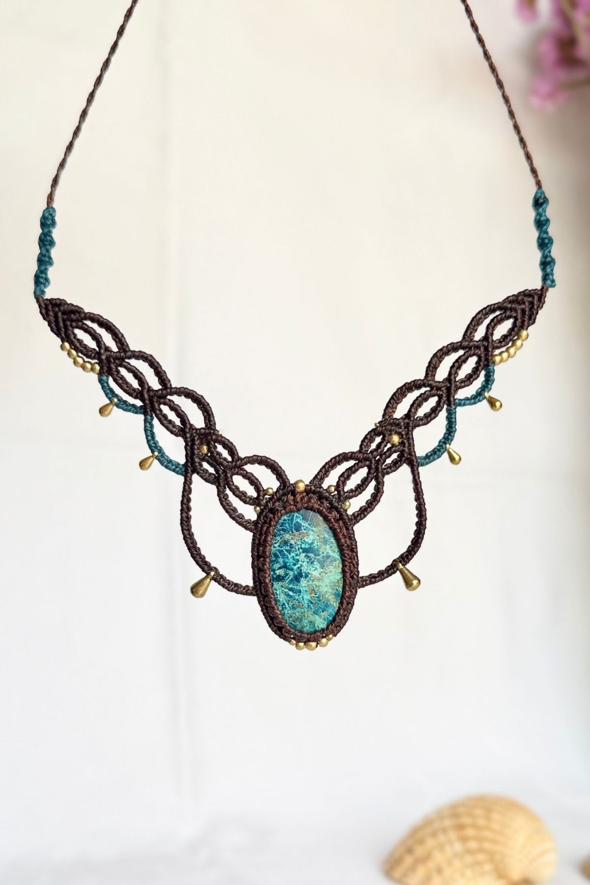 Front view of a suspended chrysocolla necklace with symmetrical brown macrame loops, turquoise accents and gold-toned beads.