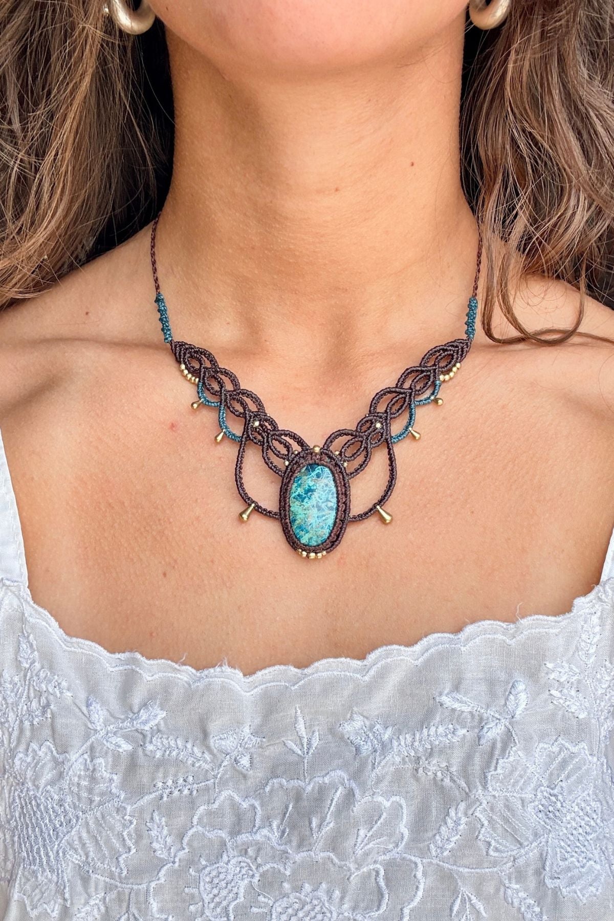 Chrysocolla macrame necklace worn with a white top, showing its V-shaped design and oval stone below the collarbone.