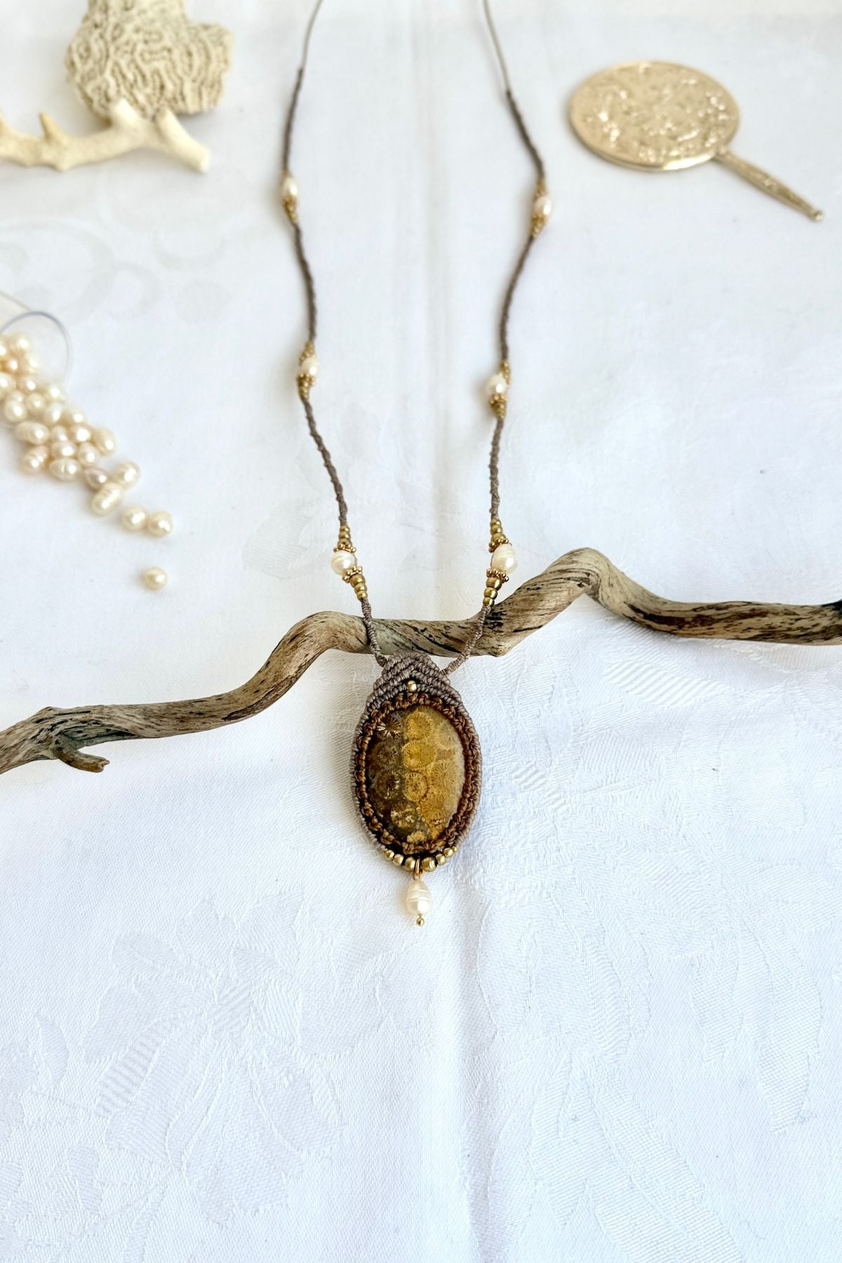 Fossil coral pendant necklace laid flat with freshwater pearls and macramé cord details, showing full design and elegant ocean inspired style