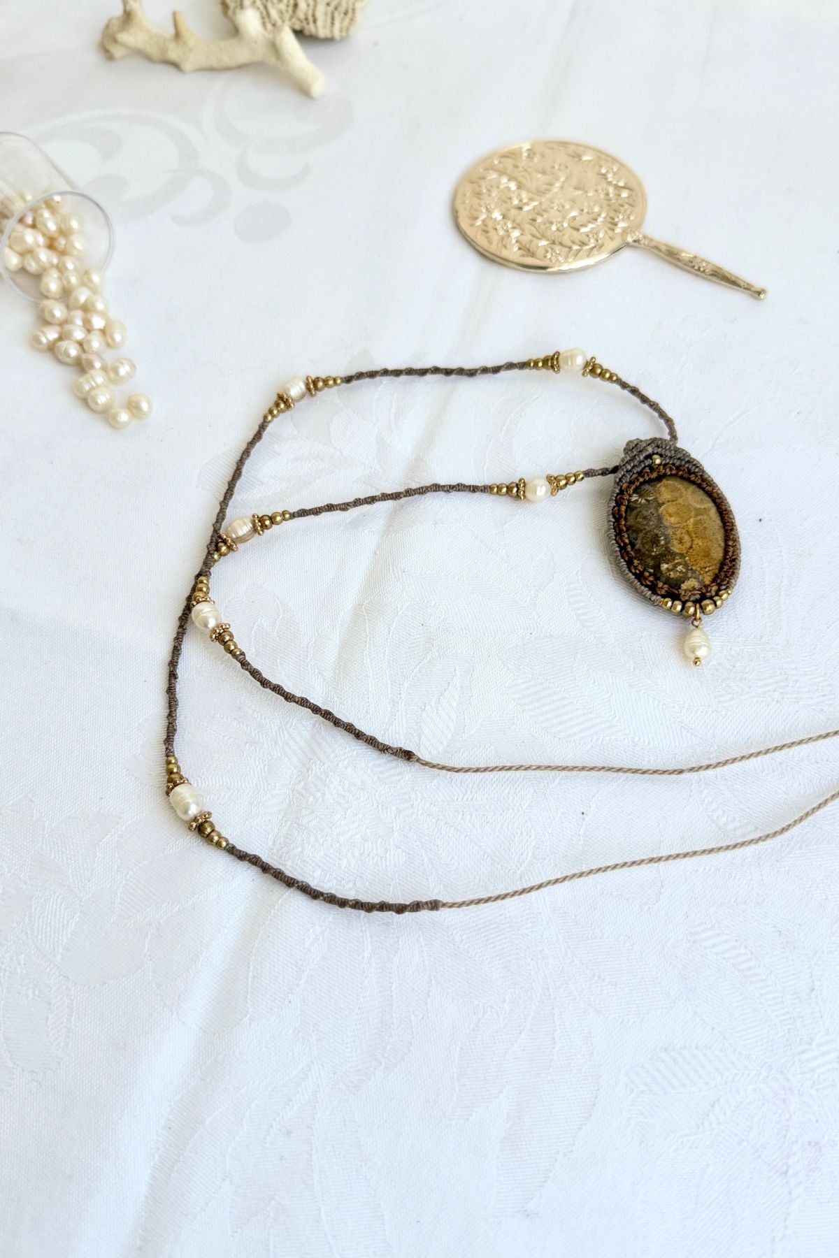 Top view of fossil coral pendant necklace laid flat showing pendant, pearl drop, and macramé cord adorned with pearls