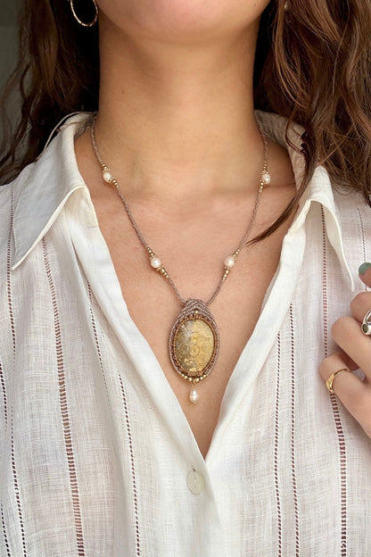Model wearing elegant fossil coral pendant necklace with freshwater pearl drop and pearls along macramé cord, ocean inspired jewelry