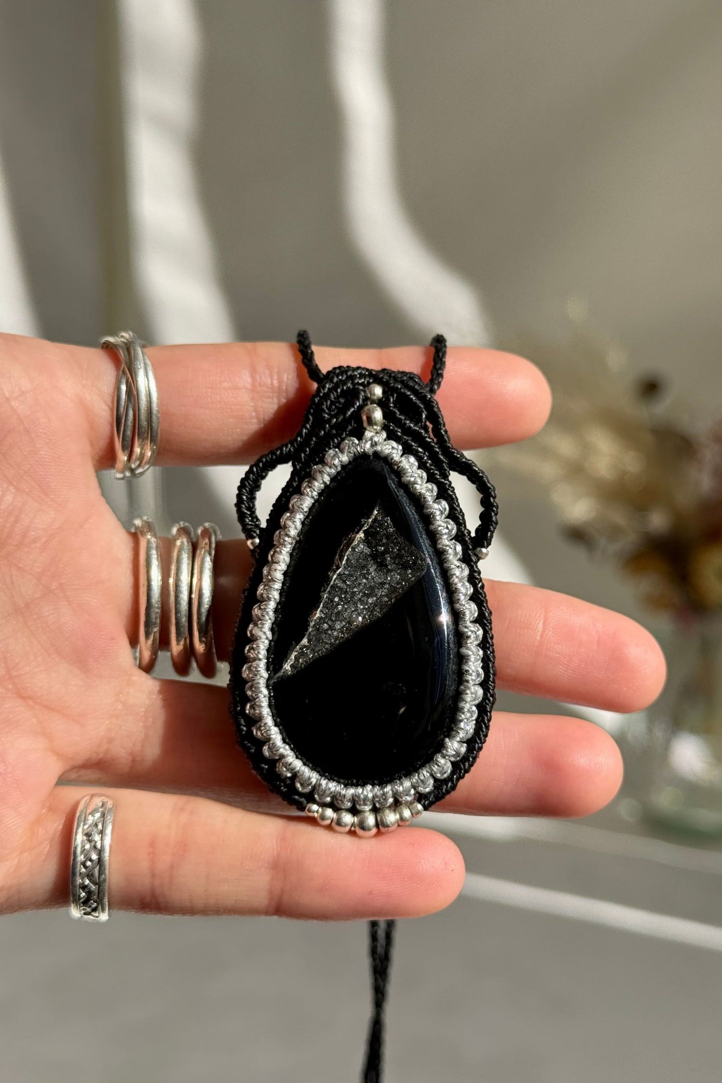 Hand holding a handmade Druzy Onyx necklace, highlighting the intricate macrame work and the natural glow of the gemstone.