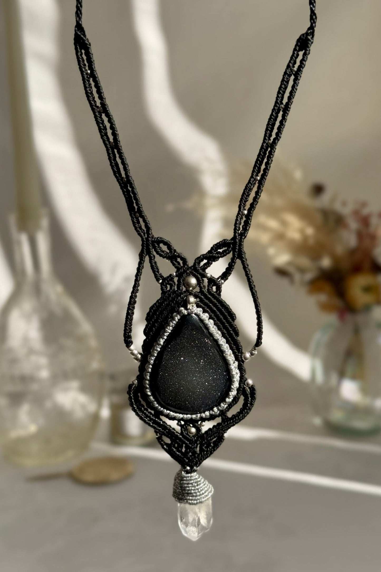 Hand holding a handmade Druzy Onyx and Clear Quartz point necklace, highlighting the intricate macrame work and the natural glow of the gemstones.