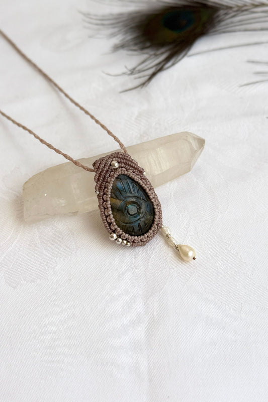 Handmade Labradorite macrame necklace with carved protective eye design, laid flat to show gemstone details and craftsmanship.