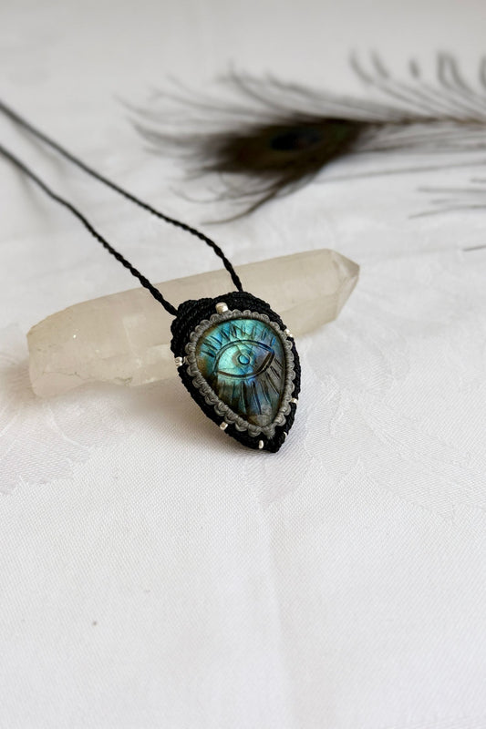 Handmade Labradorite macrame necklace with carved protective eye design, laid flat to show gemstone details and craftsmanship.