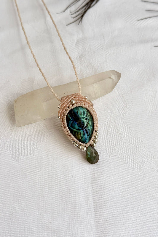 Handmade Labradorite macrame necklace with carved protective eye design, laid flat to show gemstone details and craftsmanship.