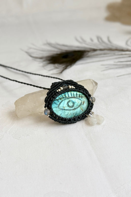 Handmade Labradorite macrame necklace with carved protective eye design, laid flat to show gemstone details and craftsmanship.