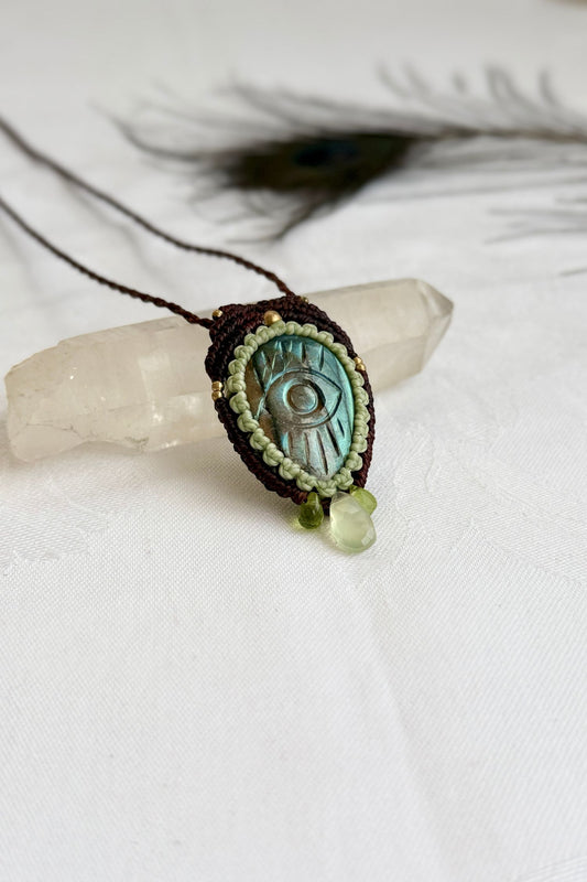 Handmade Labradorite macrame necklace with carved protective eye design, laid flat to show gemstone details and craftsmanship.