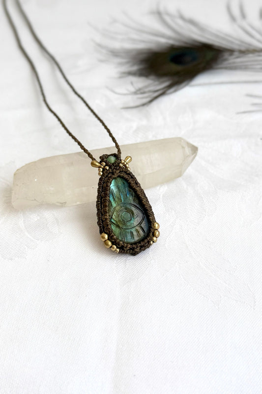 Handmade Labradorite macrame necklace with carved protective eye design, laid flat to show gemstone details and craftsmanship.