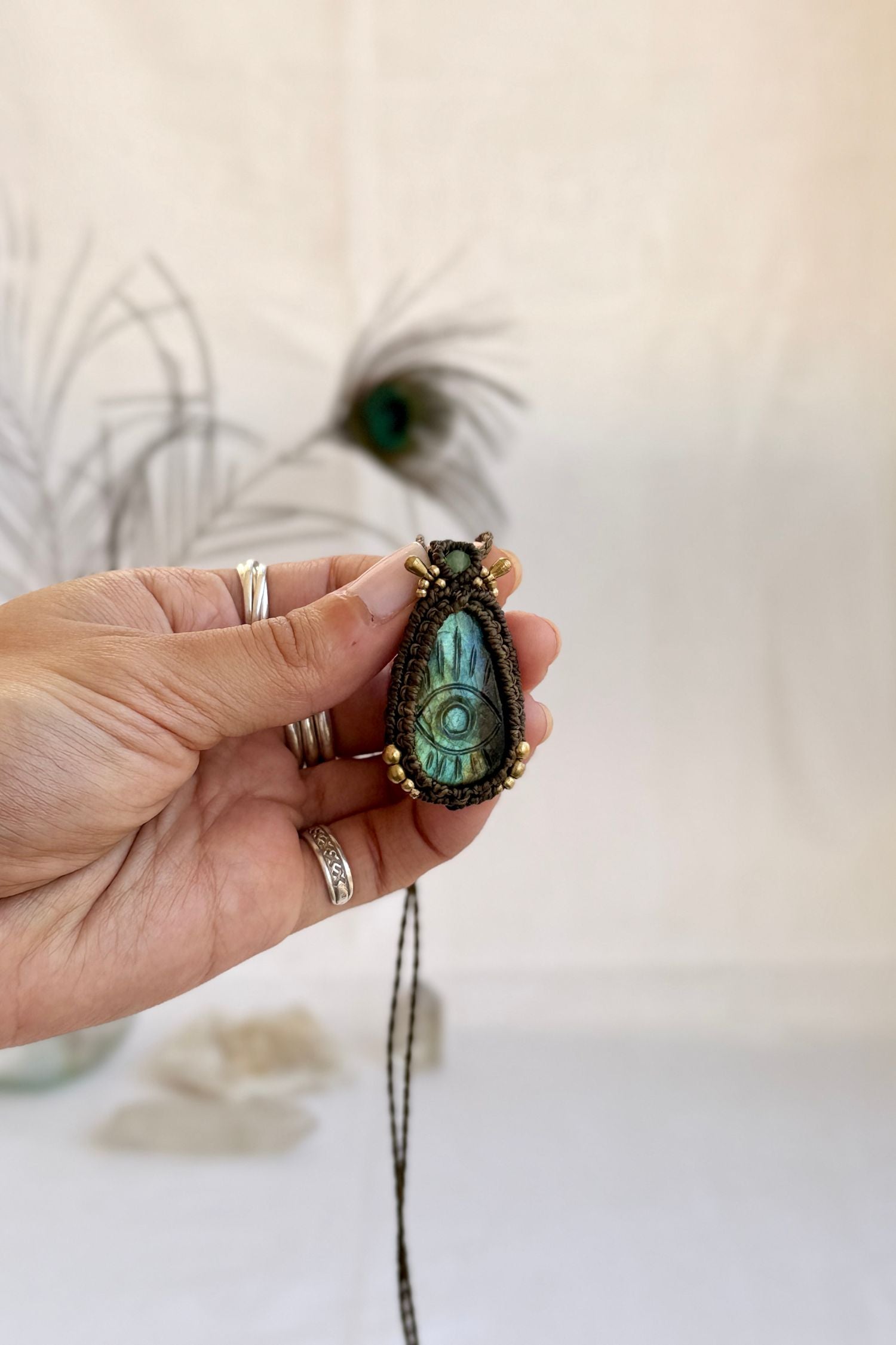 Hand holding handmade Labradorite macrame necklace with a Prehnite gemstone and golden beads accents, showing the scale and carved gemstone details.
