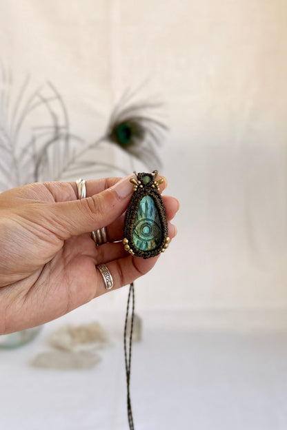 Hand holding handmade Labradorite macrame necklace with a Prehnite gemstone and golden beads accents, showing the scale and carved gemstone details.