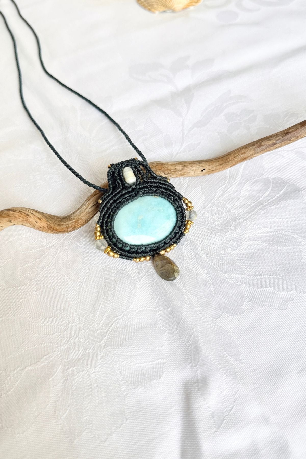 Angled view of a pale blue Larimar pendant framed in dark blue macrame, with a freshwater pearl above and a faceted Labradorite drop below.