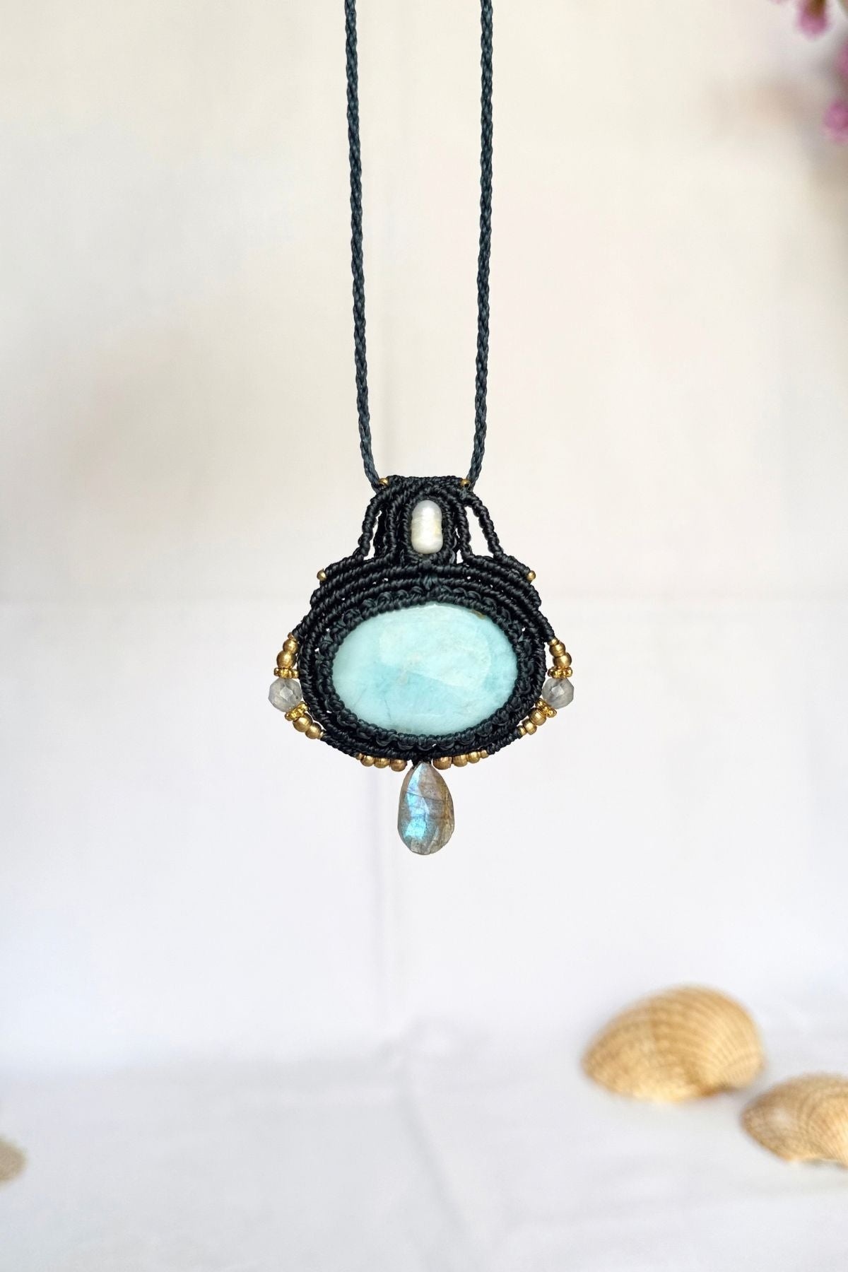 Larimar macrame pendant with a freshwater pearl and a faceted Labradorite drop showing a blue flash, hanging against a light background.