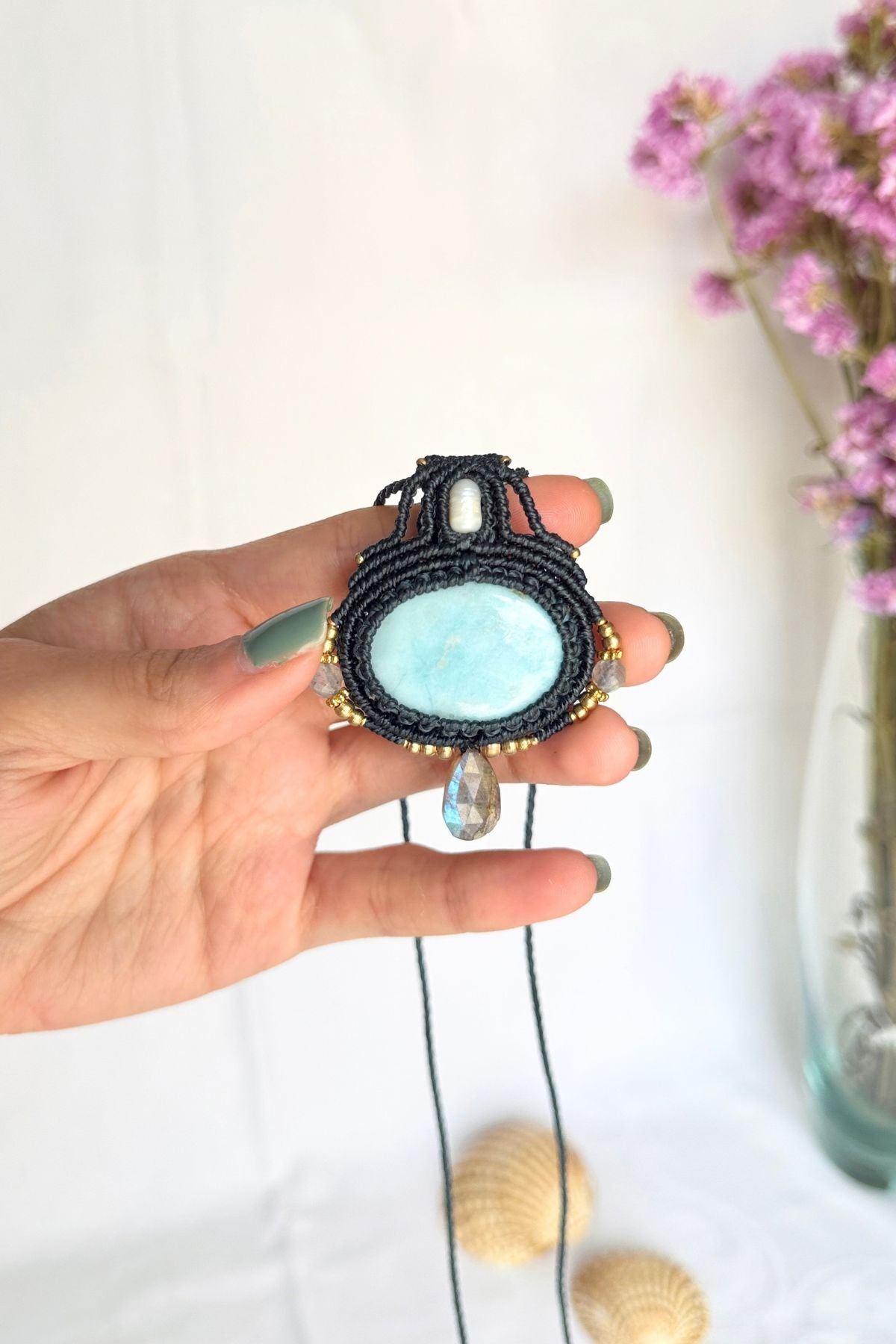 Larimar and Labradorite pendant held in a hand for scale, showing the dark blue macrame frame, freshwater pearl and gold-toned beads.