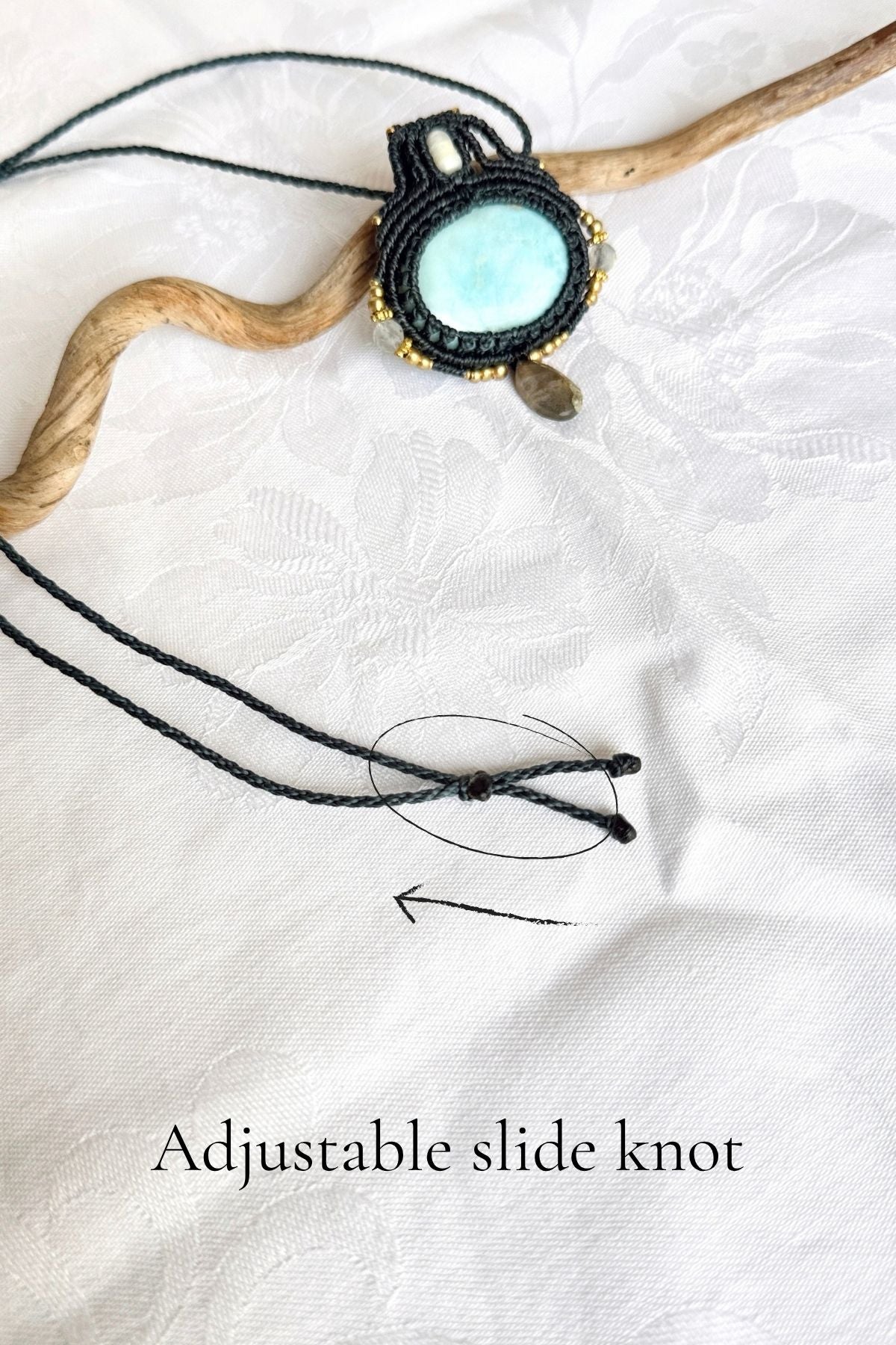 Larimar macrame necklace on white fabric, with the adjustable sliding knot circled and labelled “Adjustable slide knot”.