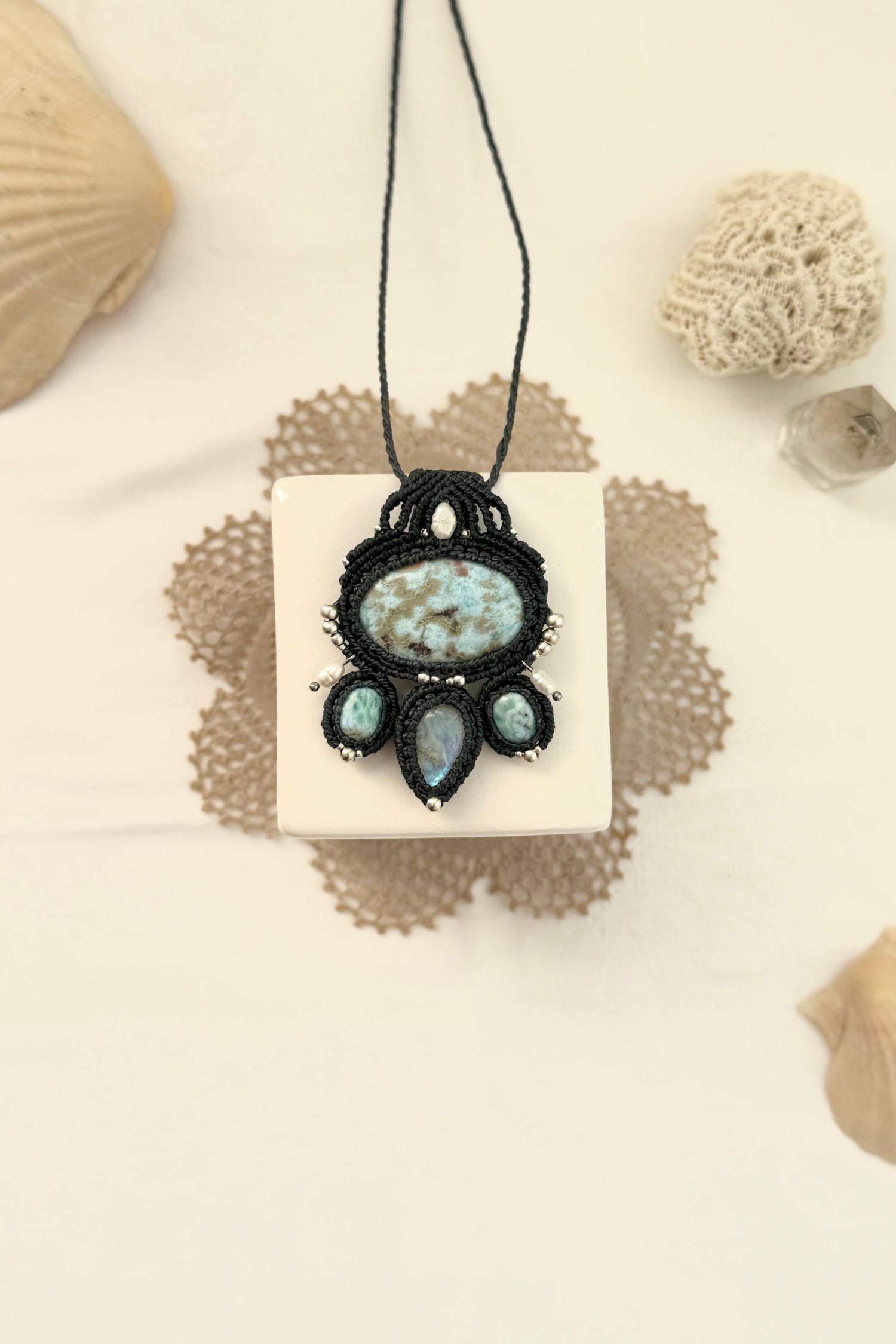 One of a kind Larimar and Moonstone macramé necklace laid flat, featuring freshwater pearls, silver details, and navy blue cord