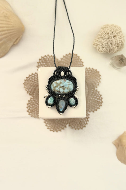 One of a kind Larimar and Moonstone macramé necklace laid flat, featuring freshwater pearls, silver details, and navy blue cord