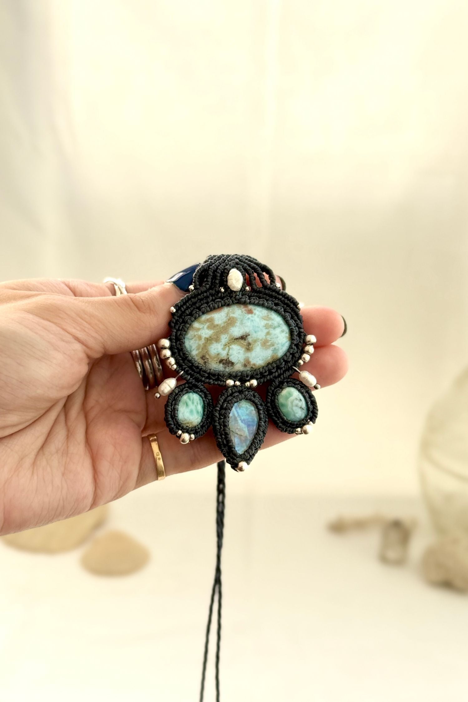 Hand holding a one of a kind Larimar macramé necklace with Moonstone, freshwater pearls, and silver bead details