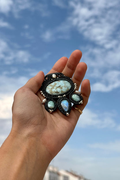 Hand holding an ocean-inspired Larimar and Moonstone necklace against a cloudy sky background, highlighting sea-blue gemstone patterns