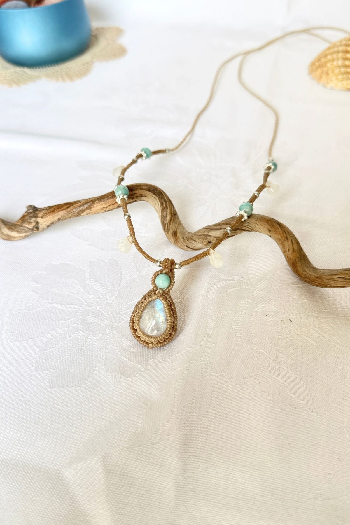 Rainbow Moonstone and Amazonite macrame necklace viewed at an angle on white fabric, with pale gemstone drops.