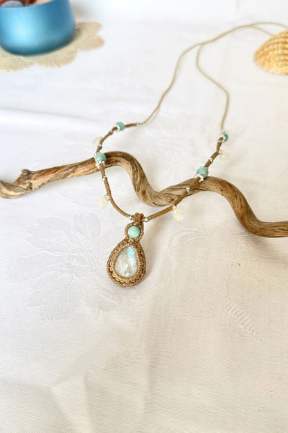 Rainbow Moonstone and Amazonite macrame necklace viewed at an angle on white fabric, with pale gemstone drops.
