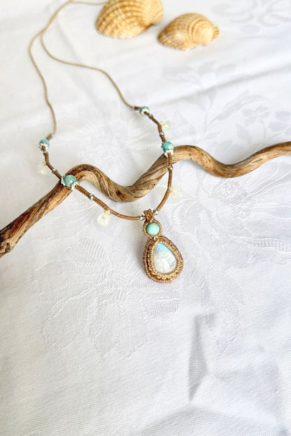 Macrame necklace arranged diagonally over a wooden branch, showing its Moonstone pendant and blue-green Amazonite beads.