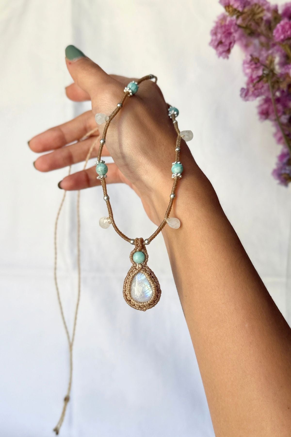 Rainbow Moonstone and Amazonite macrame necklace held in a hand, showing the pendant, gemstone beads and hanging drops.