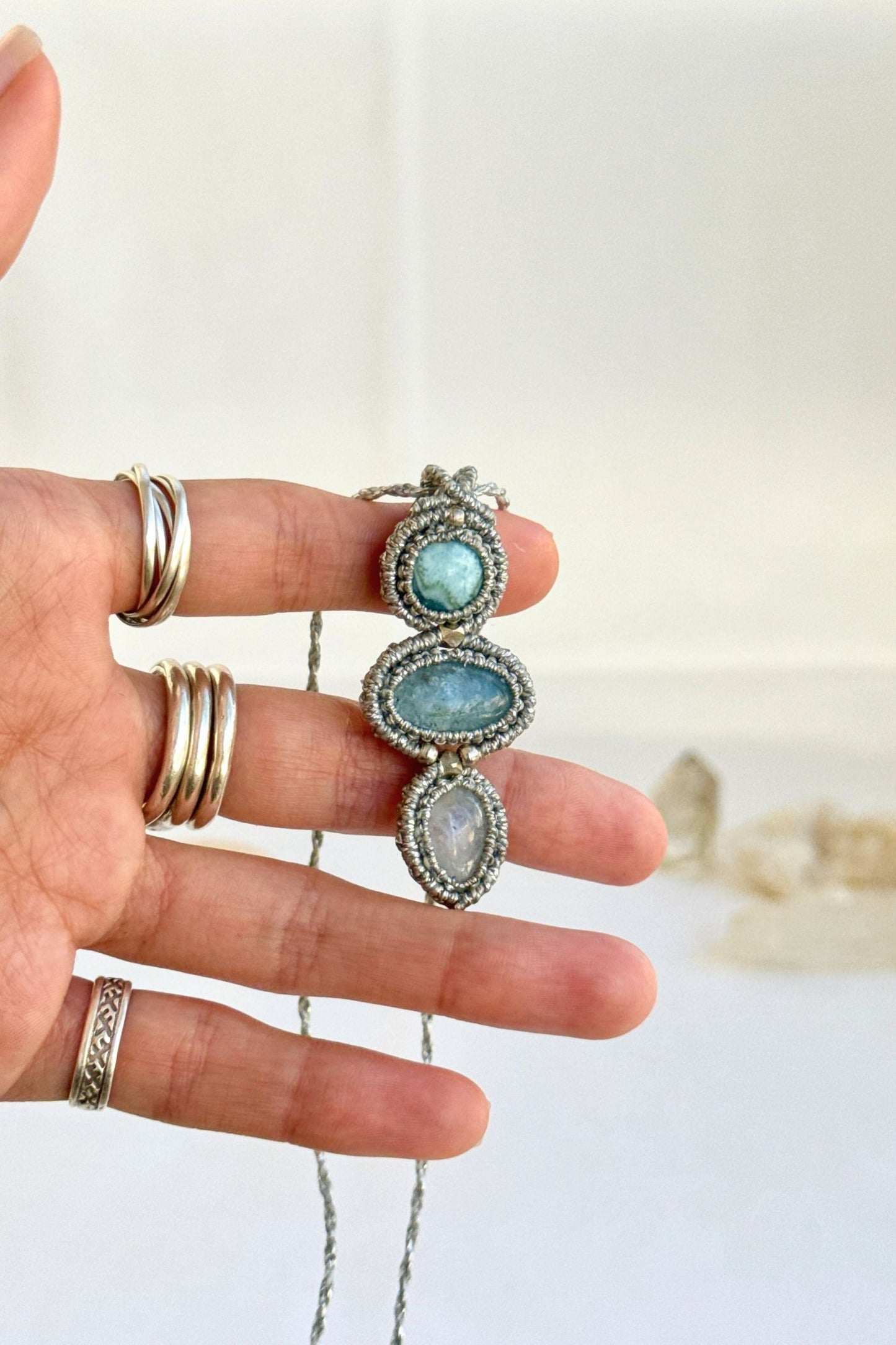 Hand holding a handmade Larimar, Aquamarine and Moonstone necklace, highlighting the intricate macrame work and the natural glow of the gemstones.
