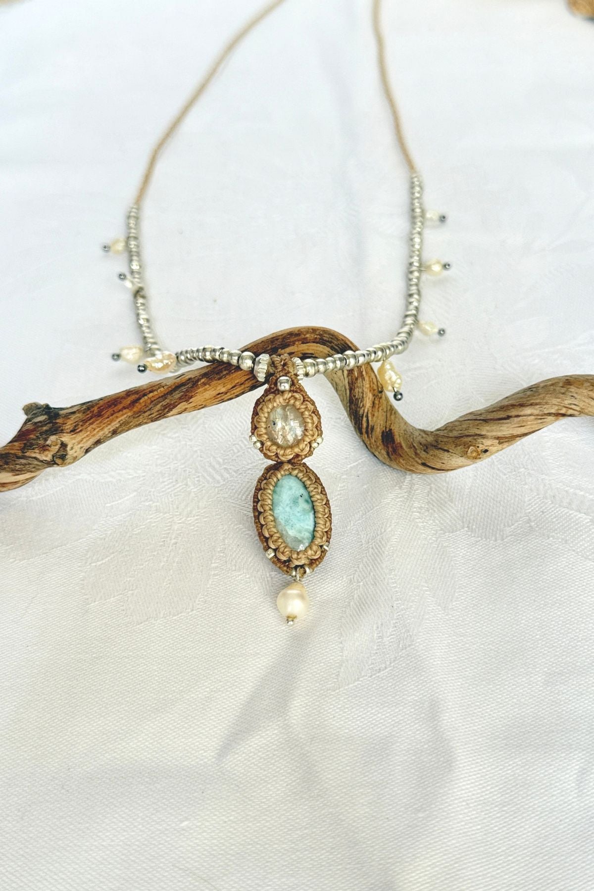 Handmade macrame necklace with Moonstone, blue Larimar and a freshwater pearl drop, displayed on a curved branch.