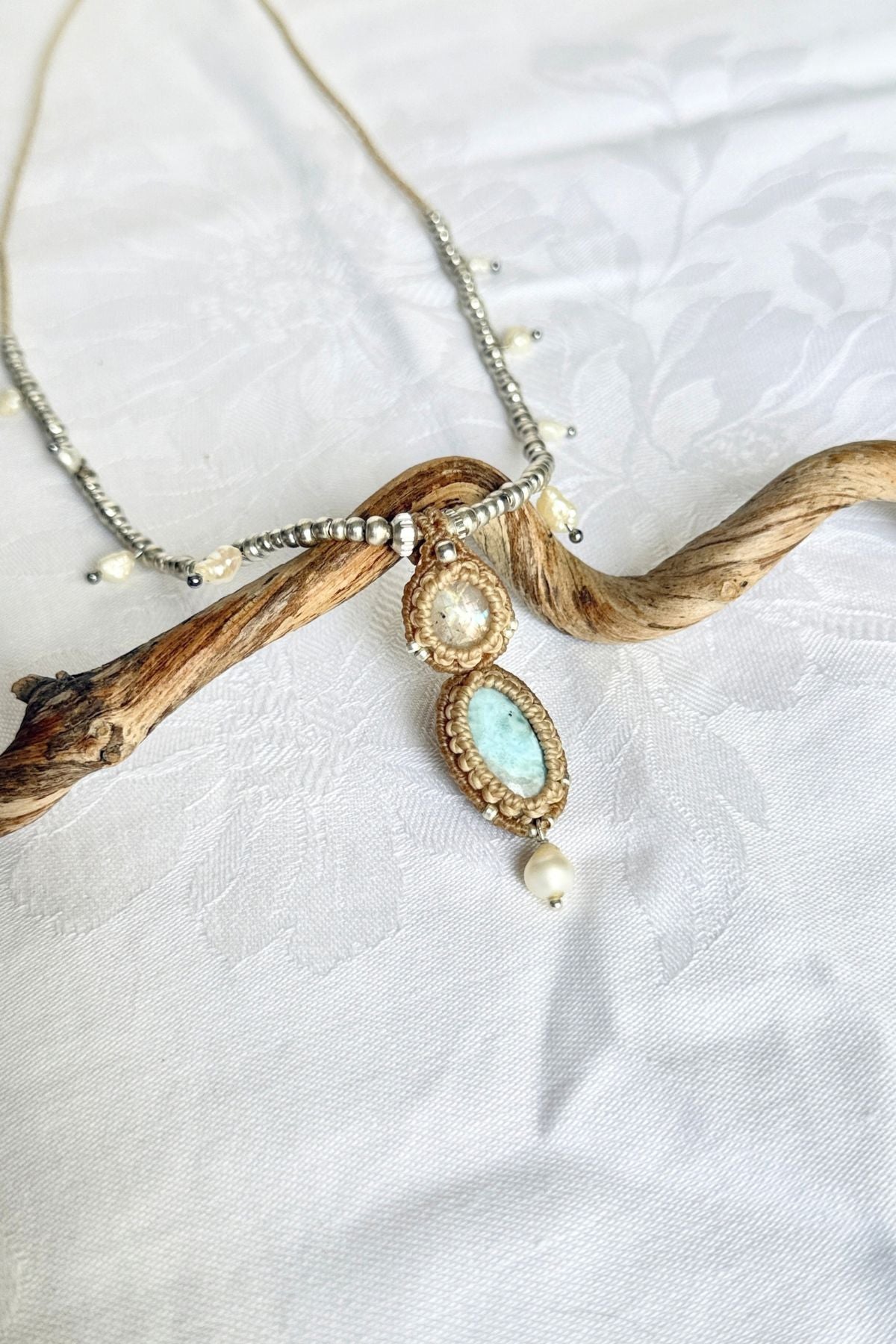 Moonstone and Larimar necklace on white fabric, showing silver-toned beads and freshwater pearls along the cord.