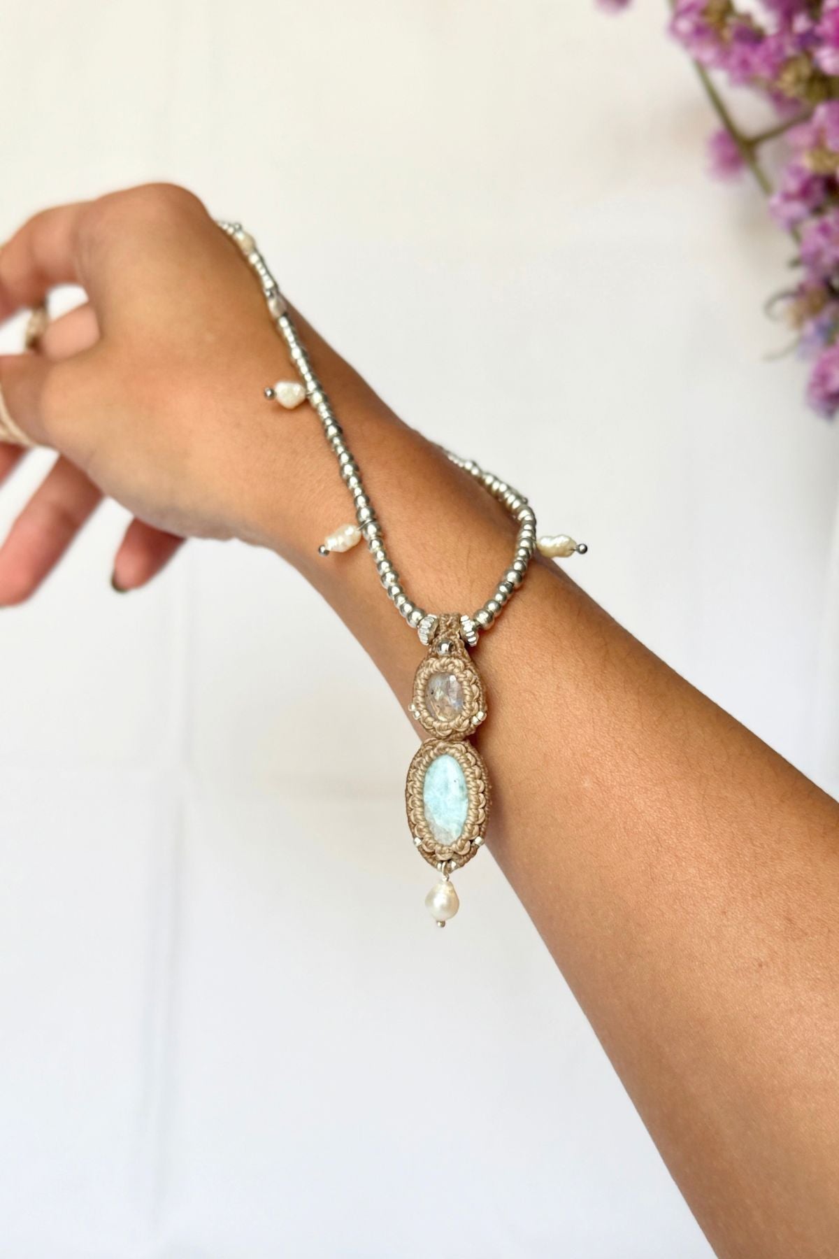 Moonstone and Larimar macrame necklace draped over a wrist, showing the pendant’s size against the skin.
