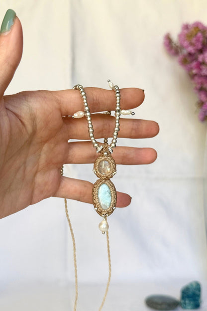 Hand holding the Moonstone and Larimar pendant, showing the macrame setting, freshwater pearl drop and beaded cord.