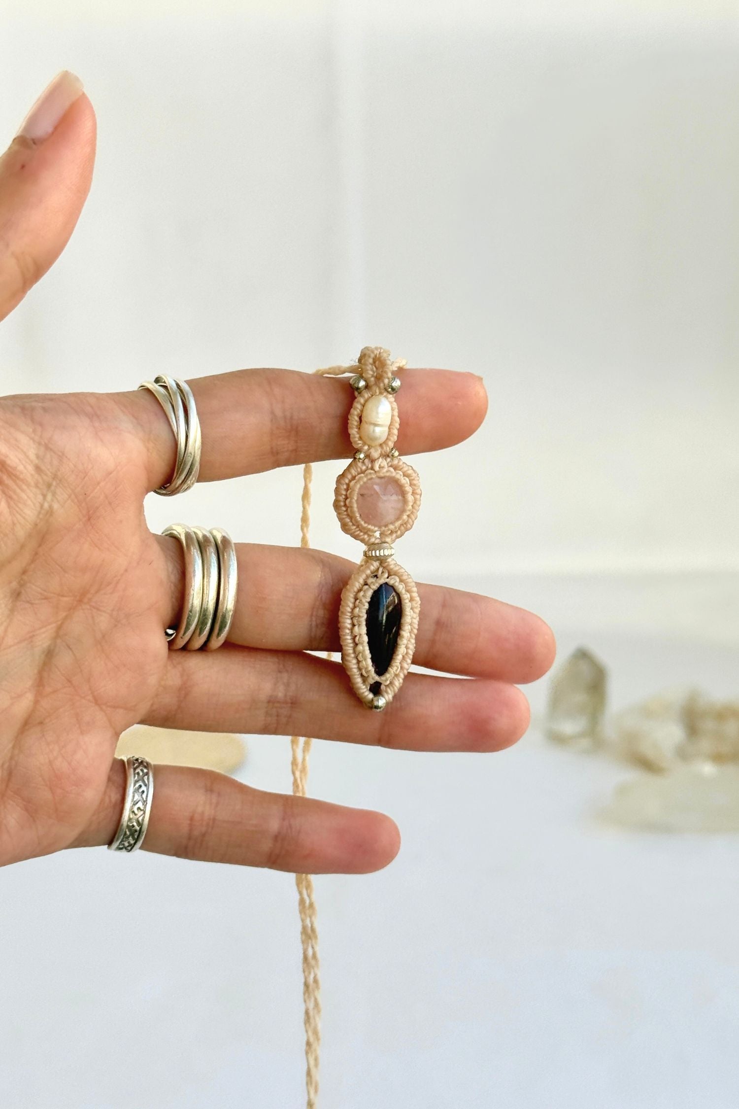 Hand holding a handmade Freshwater Pearl, Rose Quartz and Amethyst necklace, highlighting the intricate macrame work and the natural glow of the gemstones.