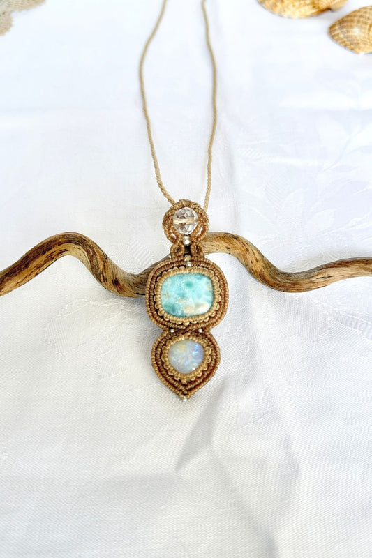 Larimar, Moonstone and faceted clear quartz pendant in beige macrame, displayed on a curved branch.