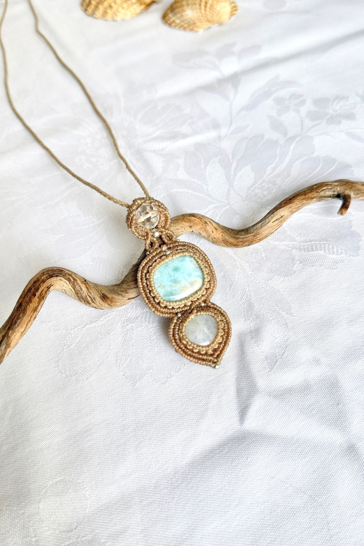 Angled view of the macrame pendant, showing the blue Larimar patterns, clear quartz facets and round Moonstone.