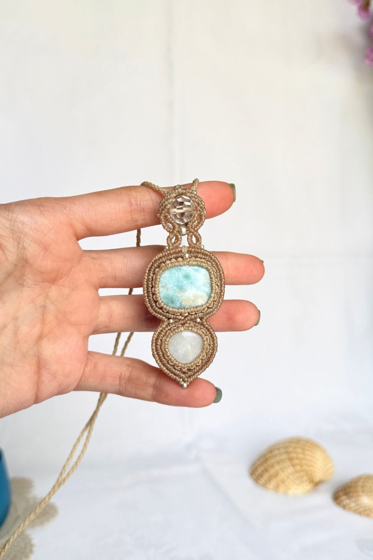 Hand holding the Larimar, Moonstone and quartz pendant, showing its size and the detailed macrame setting.